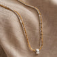 A delicate double-strand necklace with one gold and one silver chain, featuring a small silver ring charm, displayed on a textured beige linen fabric.