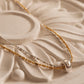 A close-up of a delicate two-tone necklace with gold and silver chains, featuring a polished silver bead pendant, resting on a textured beige stone surface.