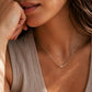 A close-up lifestyle shot of a woman wearing a delicate gold chain necklace with a small round pendant, paired with a beige ribbed top.