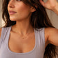 A woman wearing a delicate gold chain necklace with a small central bead, styled with a lavender ribbed tank top.