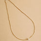 A delicate gold chain necklace with a small silver round pendant, displayed on a solid beige background.