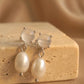 A pair of dainty silver stud earrings with moonstone and freshwater pearl drop crafted in 925 sterling silver displayed on an aesthetic beige color stone, minimal wedding earrings.