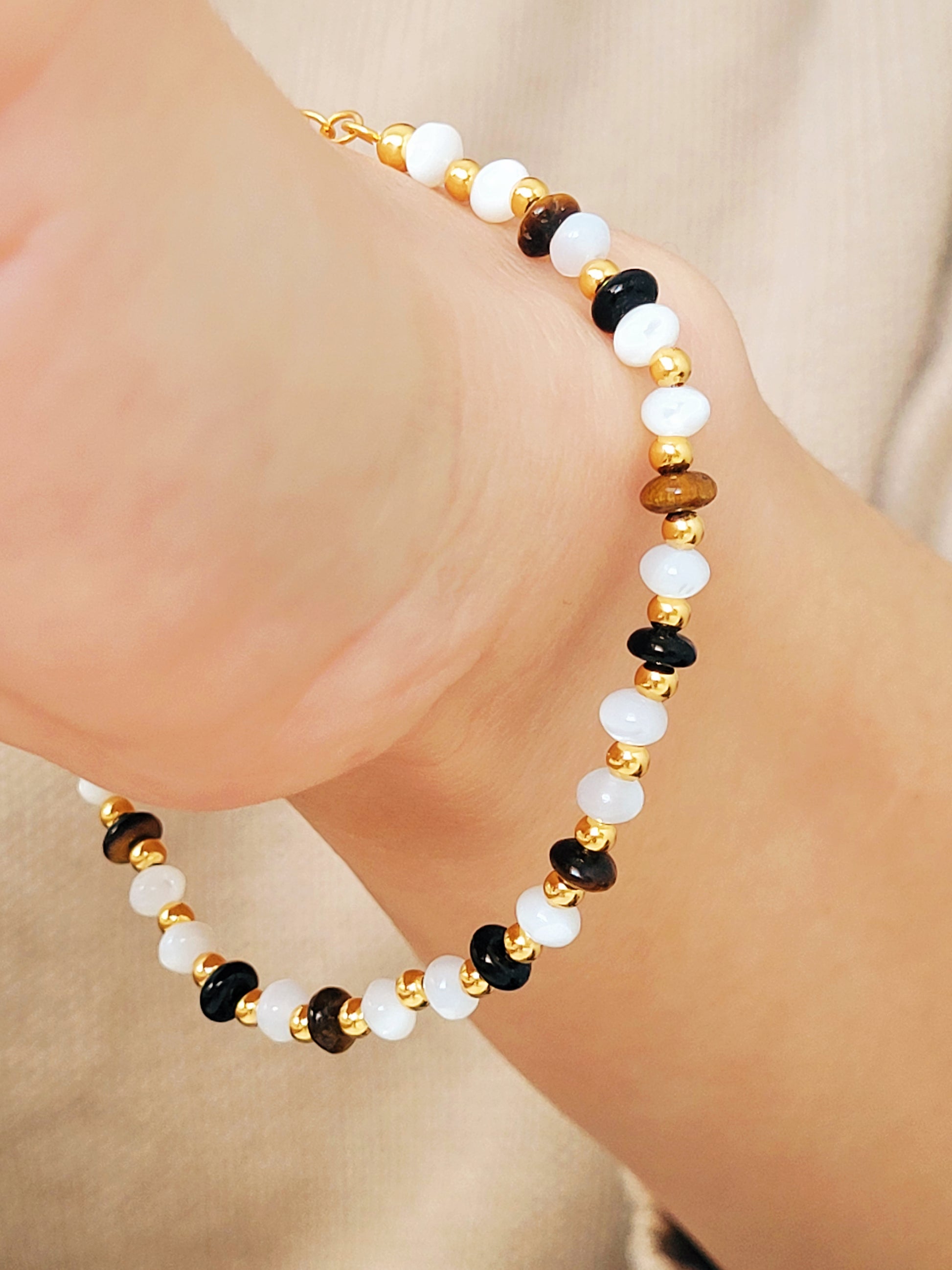A gemstone bracelet featuring tiger's eye, mother of pearl, and black onyx beads with 22k gold vermeil accents, worn on wrist.