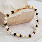 A natural stone bracelet featuring tiger's eye, mother of pearl, and black onyx beads with 22k gold vermeil accents lied on a stone