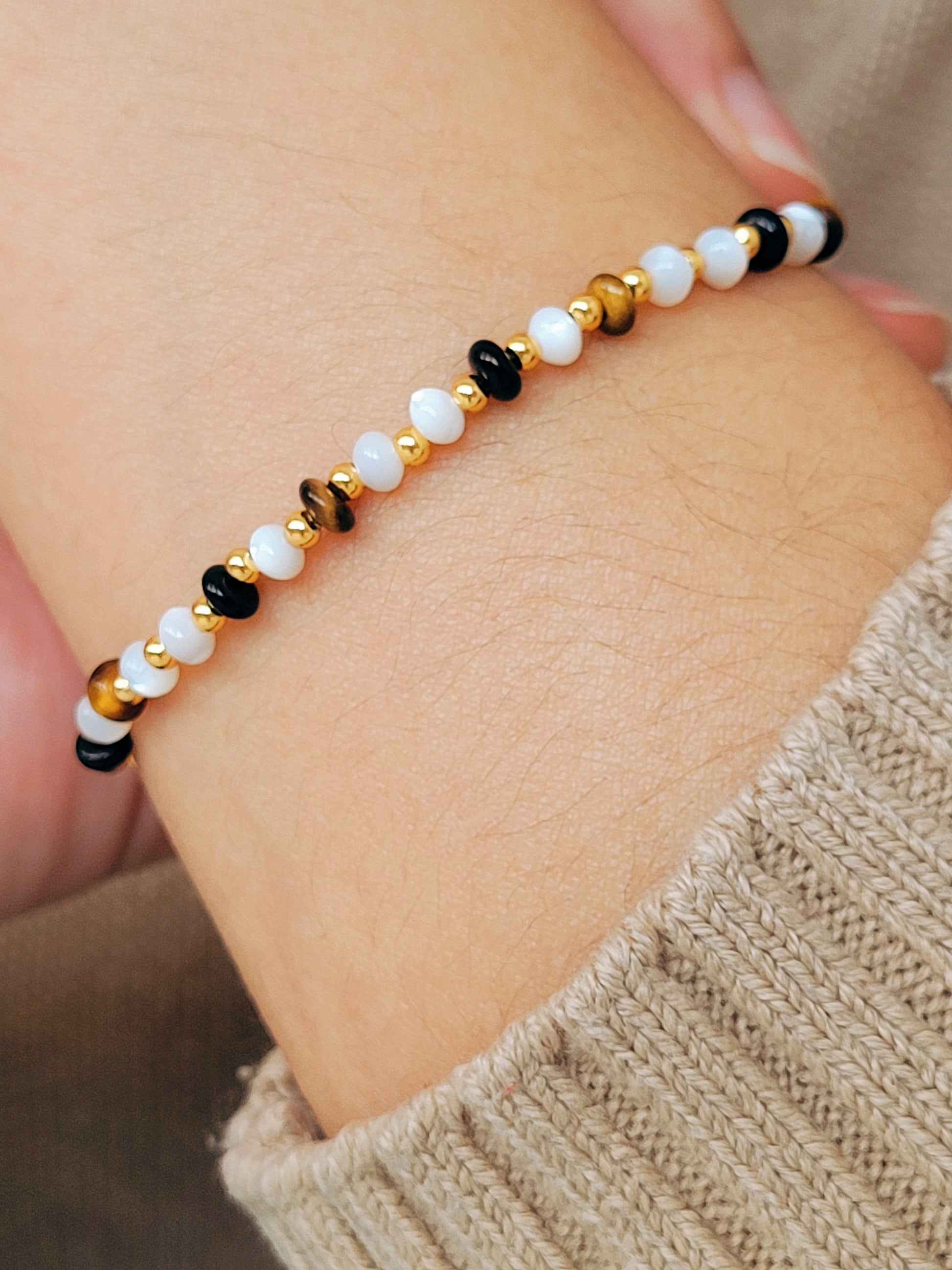Model wearing a gemstone bracelet featuring tiger's eye, mother of pearl, and black onyx beads with 22k gold vermeil accents