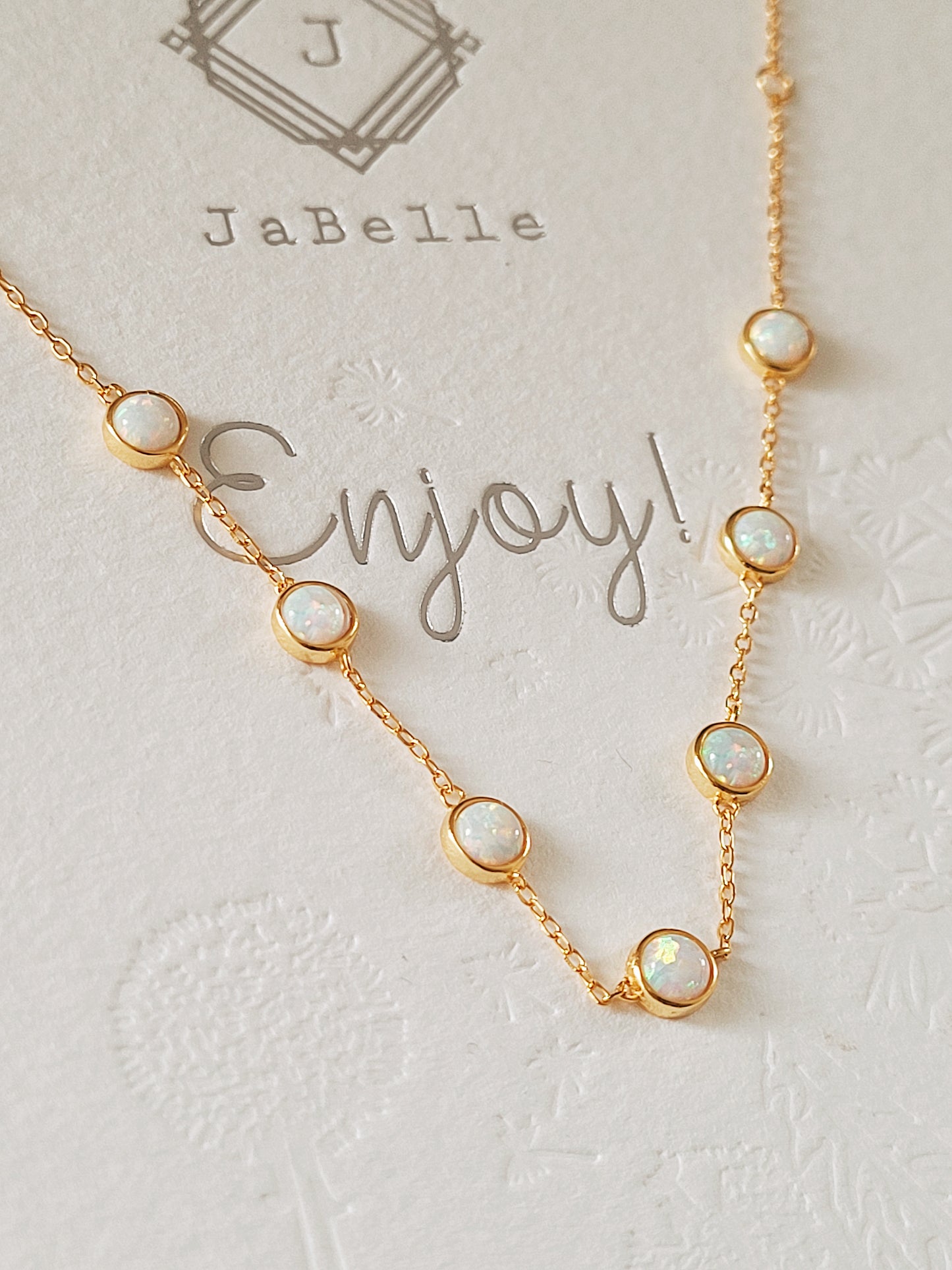 A gold chain bracelet with seven iridescent round opal stones, displayed on a JaBelle Jewellery thank you card. Complements the elegance of their opal bracelet.