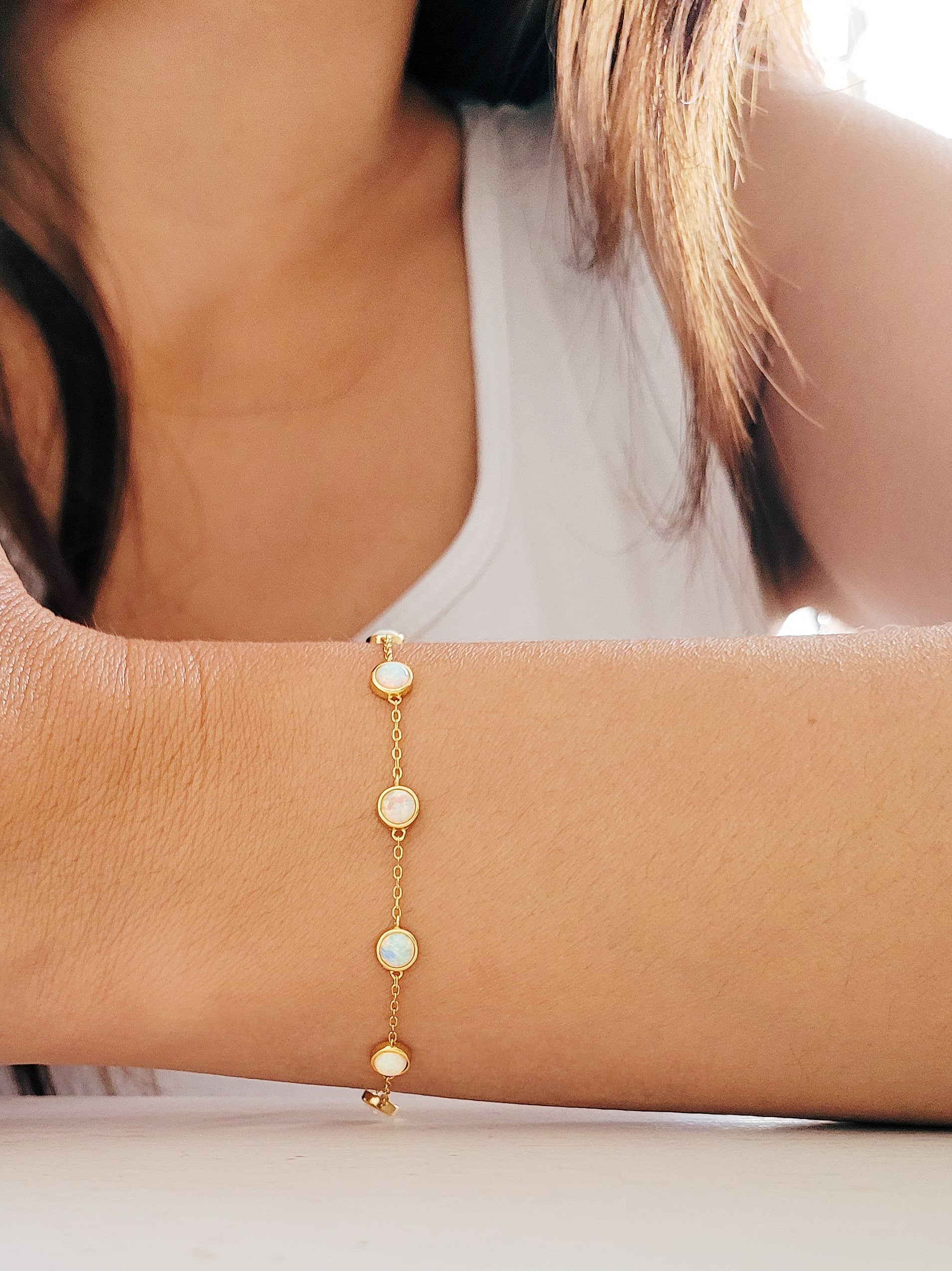 A woman elegantly wearing a gold opal bracelet and earrings, emphasizing her refined taste in jewelry and fashion.