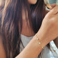 A woman elegantly holds a mirror, showcasing her stunning gold-plated opal bracelet with white opal stones.