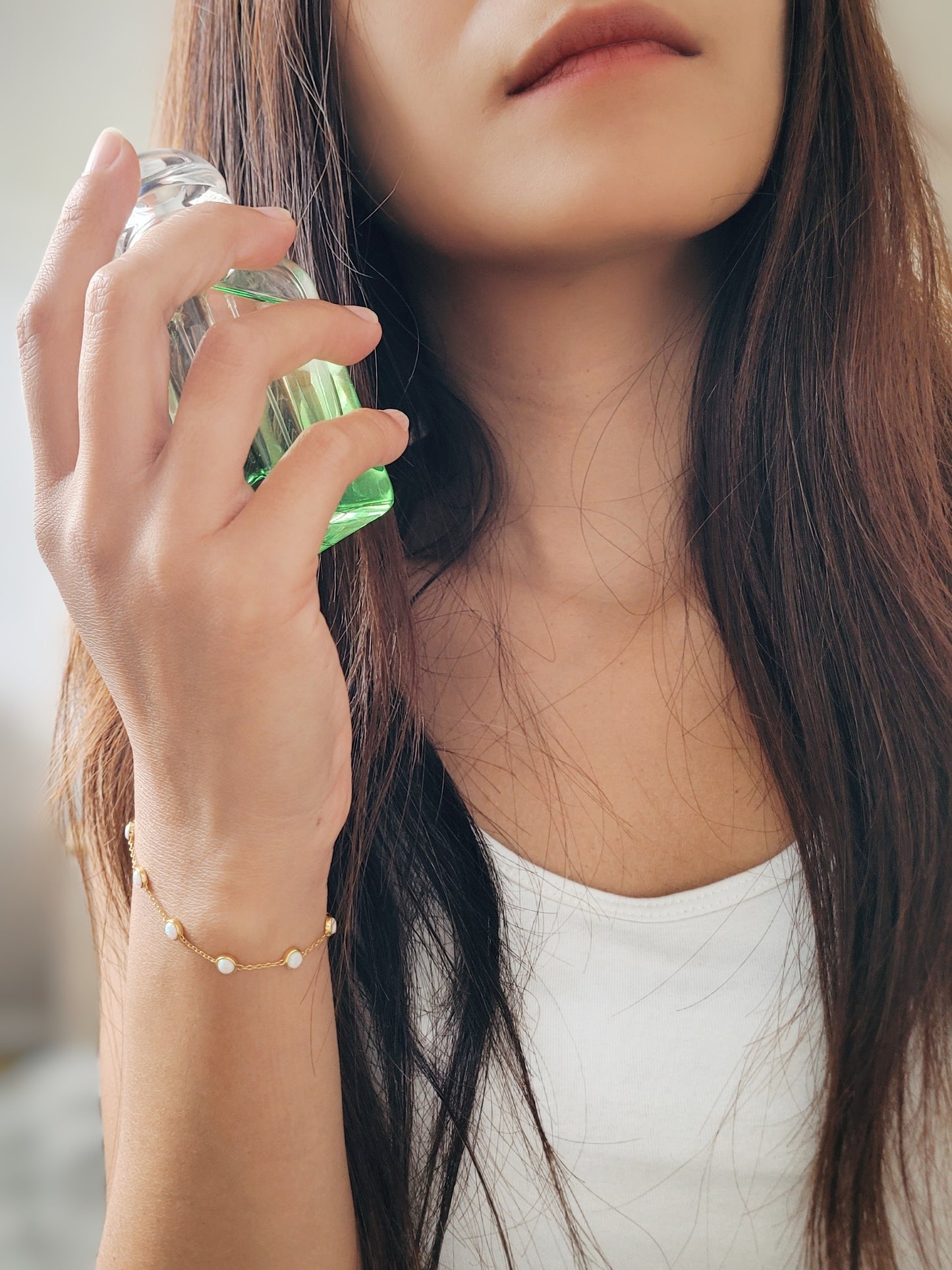 A woman elegantly holds a perfume bottle, showcasing her stunning gold-plated opal bracelet with white opal stones.