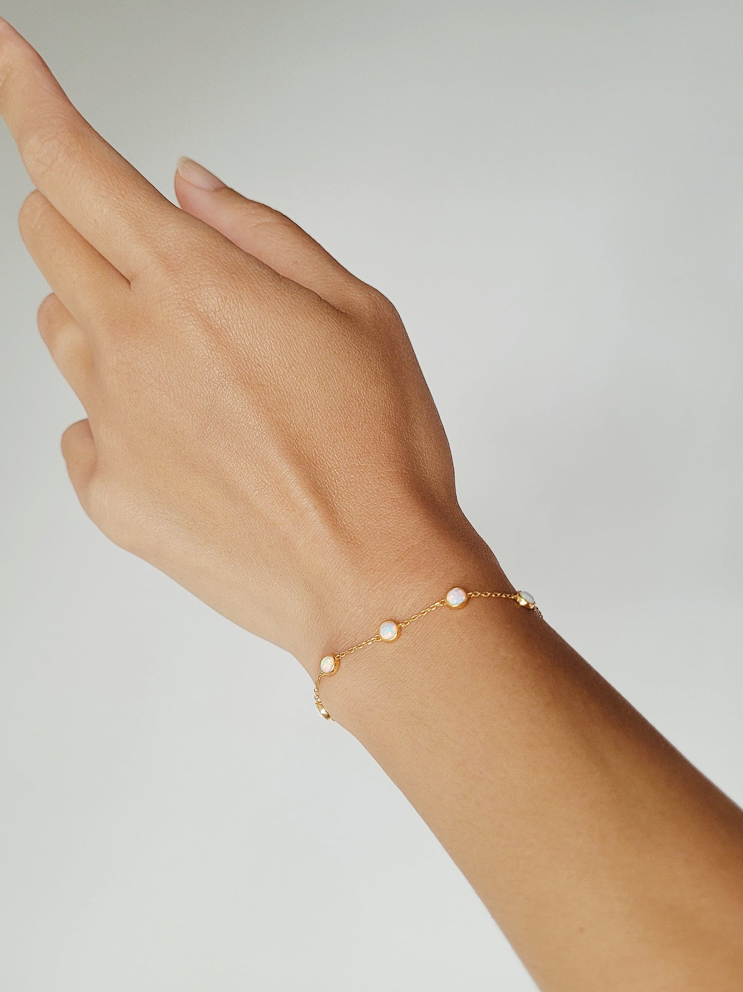 A woman hand adorned with a gold fire opal bracelet.