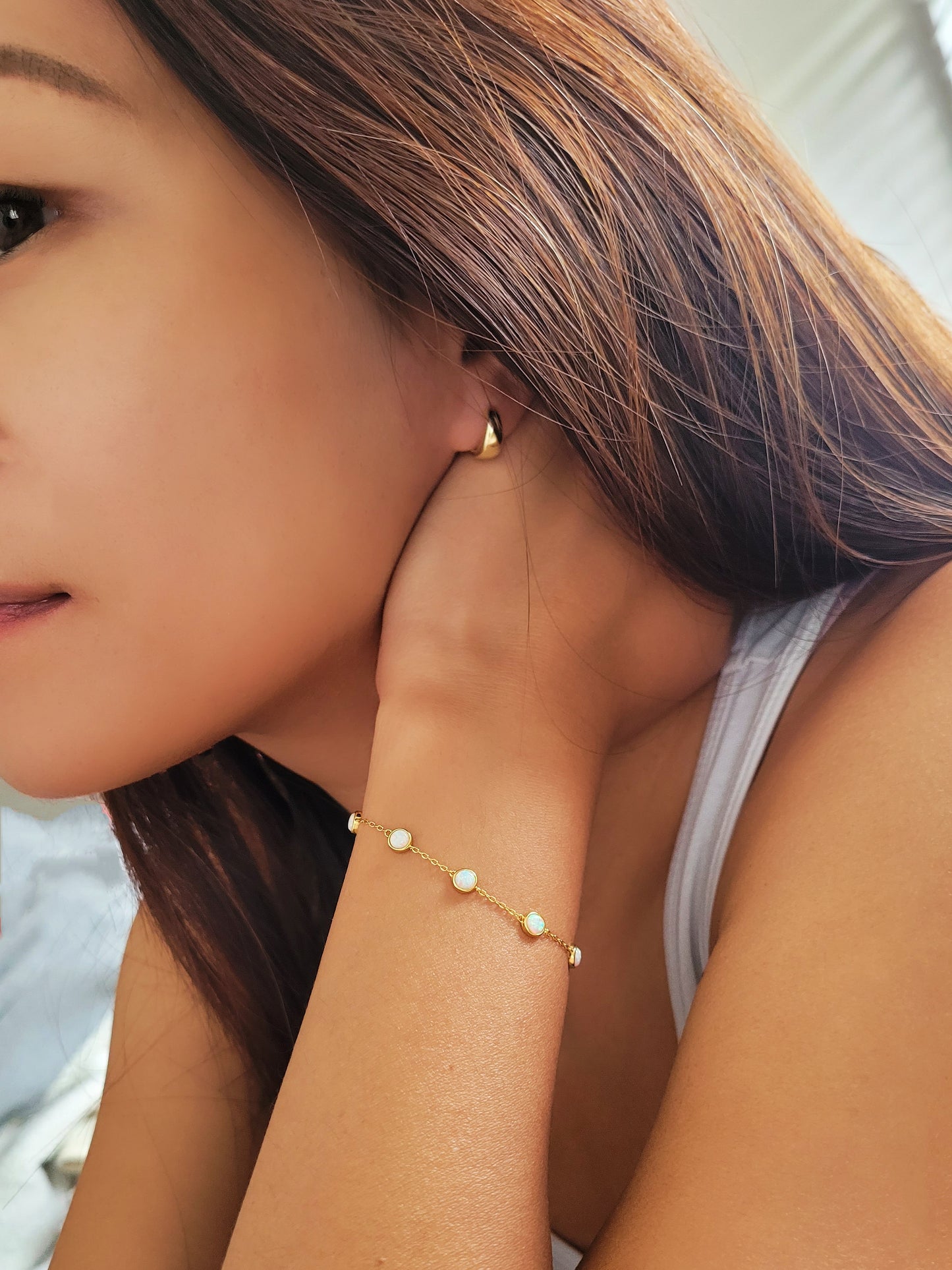 A woman displaying a gold opal bracelet and earrings, highlighting her sophisticated style and the shine of her accessories.