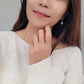 A chic woman wearing a white sweater, featuring beautiful earrings and a refined open cross ring, radiating luxury and grace.