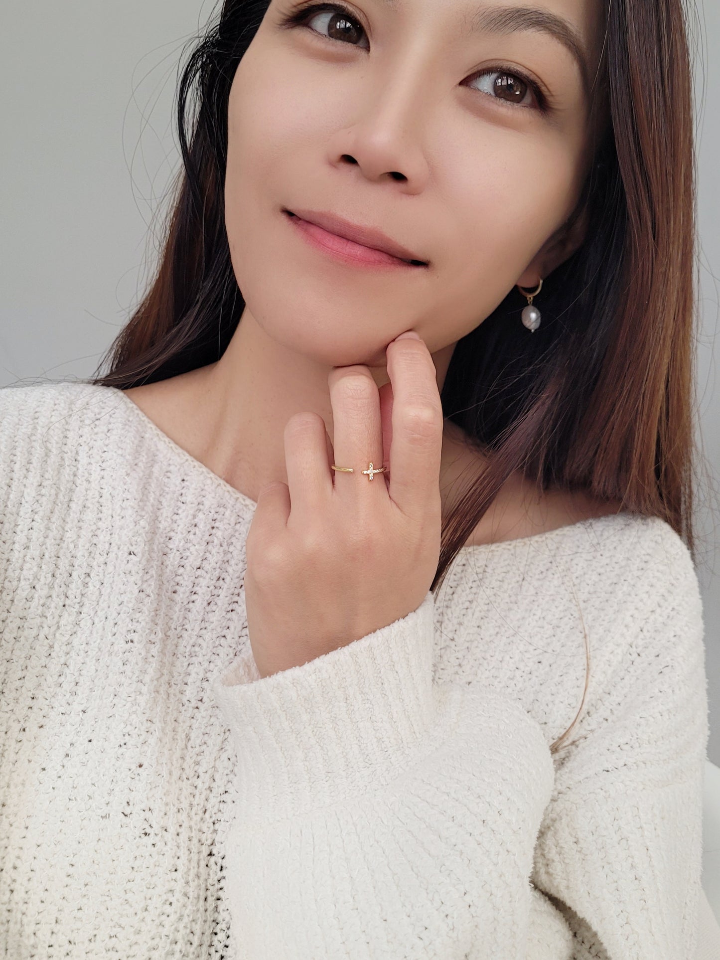 A chic woman wearing a white sweater, featuring beautiful earrings and a refined open cross ring, radiating luxury and grace.