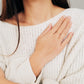 A chic woman wearing a white sweater, featuring beautiful earrings and a refined open cross ring, radiating luxury and grace.