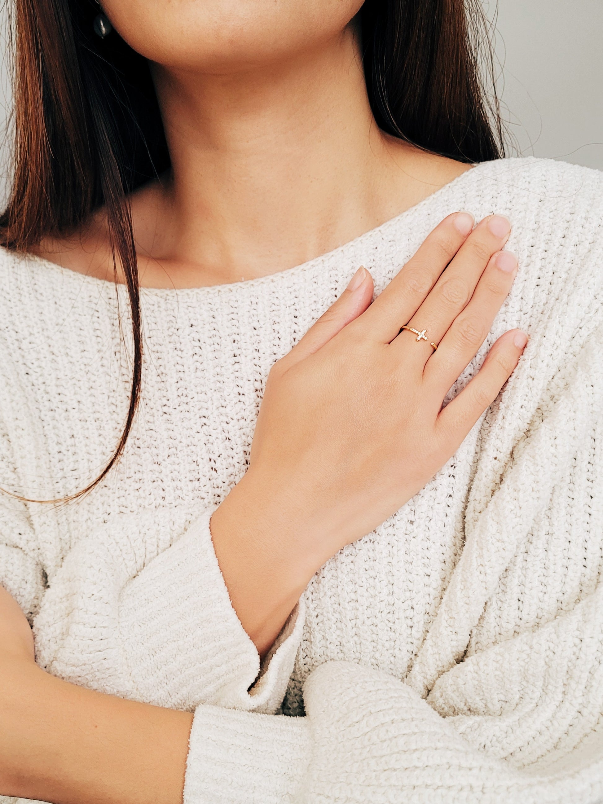 A chic woman wearing a white sweater, featuring beautiful earrings and a refined open cross ring, radiating luxury and grace.