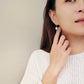 A woman elegantly adorned in a white sweater, showcasing stunning earrings and an exquisite open cross ring.