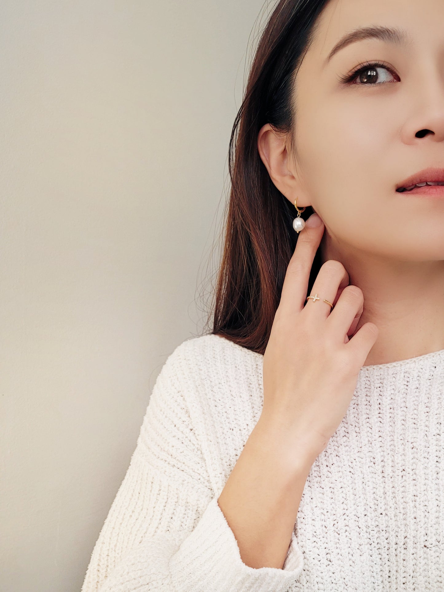 A woman elegantly adorned in a white sweater, showcasing stunning earrings and an exquisite open cross ring.