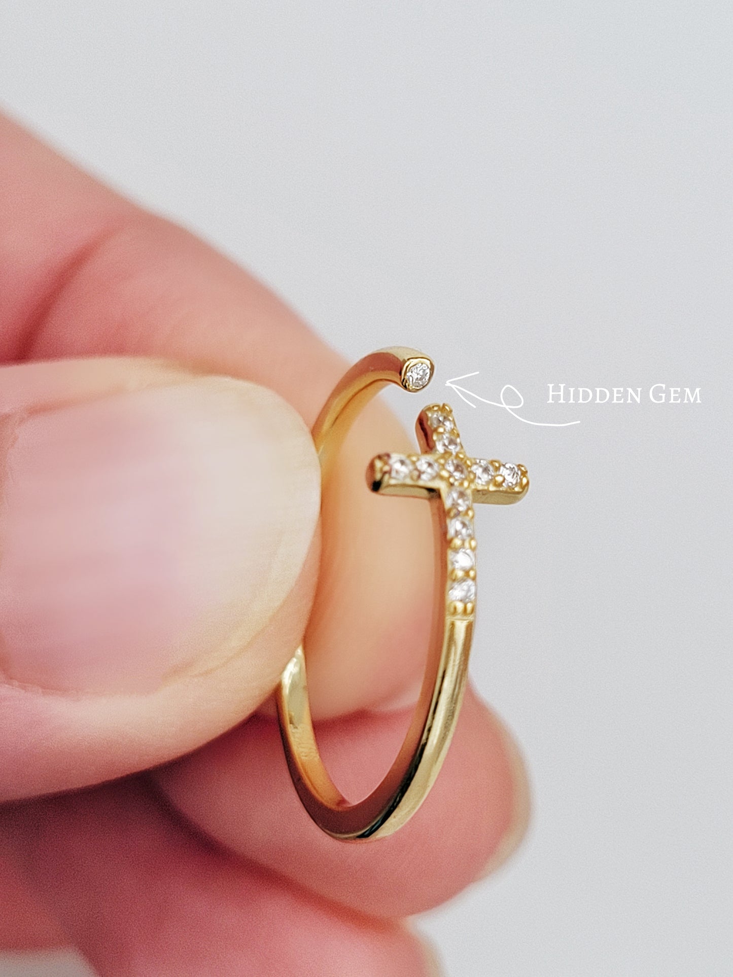 A delicate gold cross ring featuring an open cross design, adorned with a hidden diamond gem for a touch of elegance.