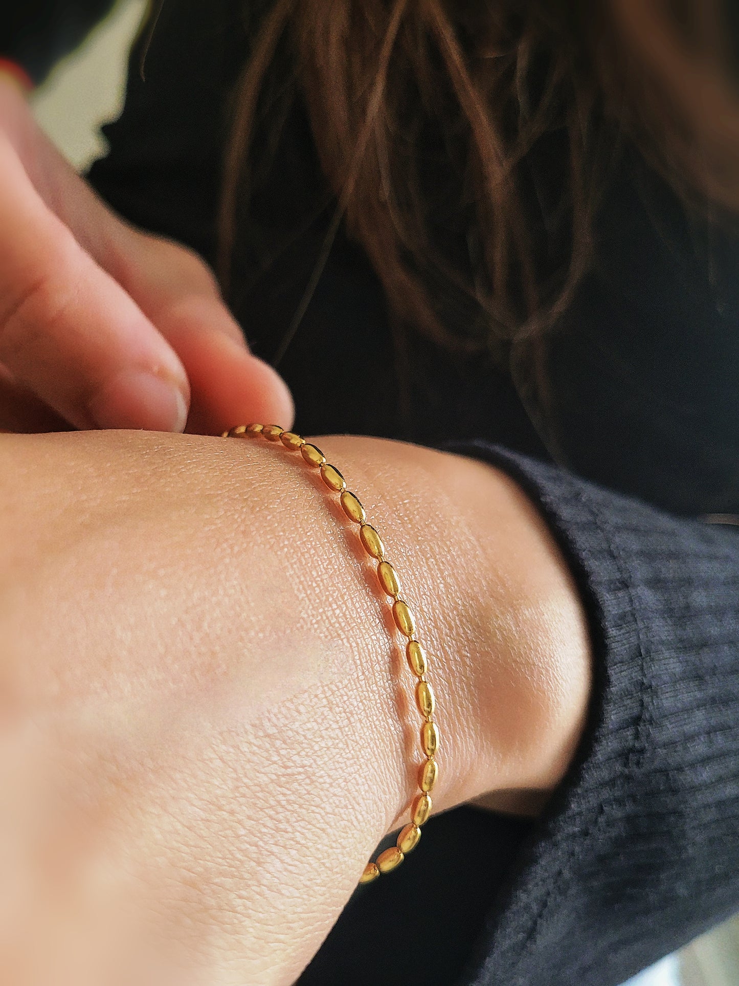 Close-up of a woman&#39;s hand wearing the elegant and dainty gold-plated oval beaded bracelet, highlighting its lustrous finish and intricate bead arrangement.