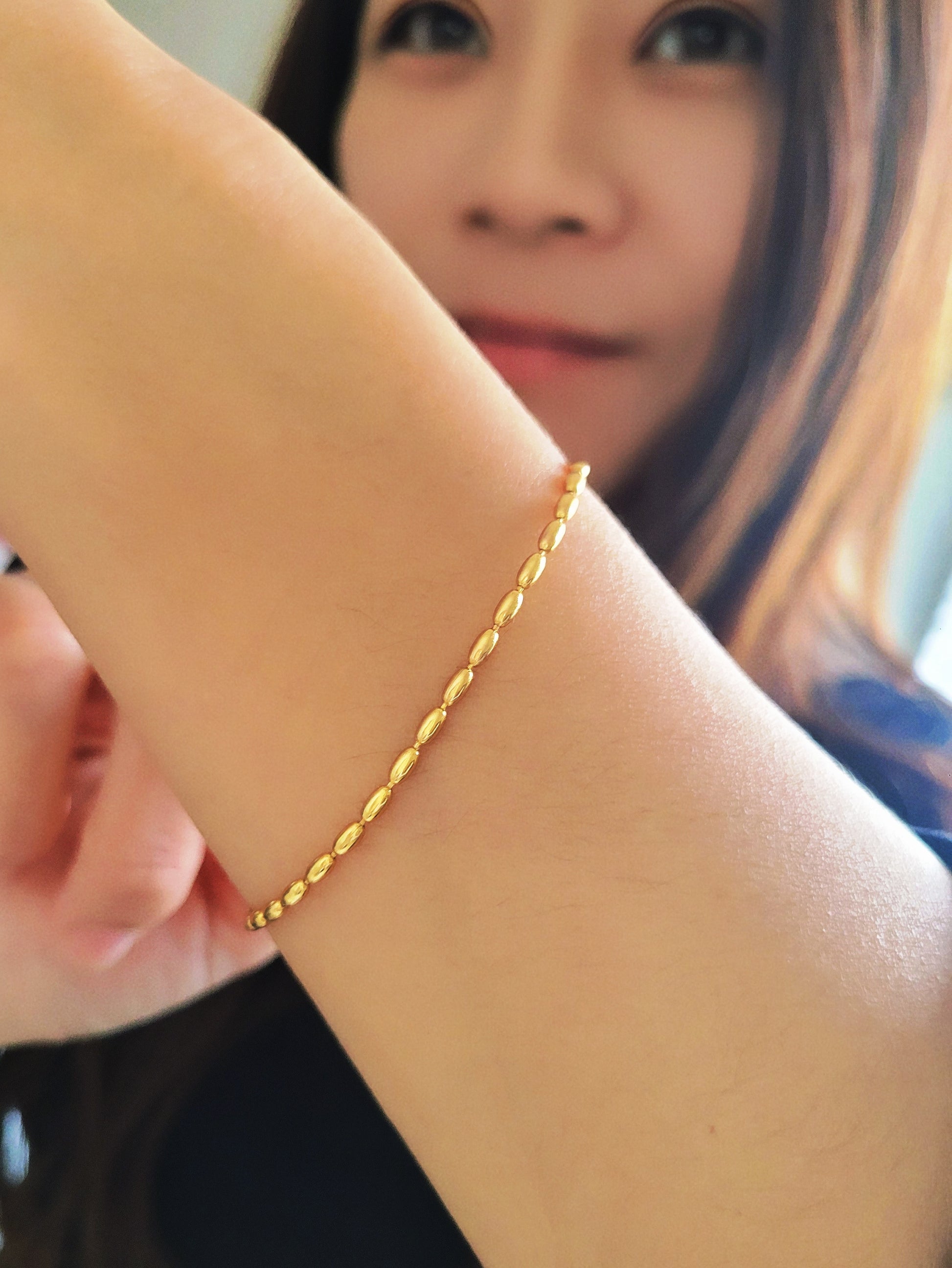 Close-up of a woman's hand wearing the elegant and dainty gold-plated oval beaded bracelet, highlighting its lustrous finish and intricate bead arrangement.