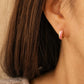 Close up of a woman wearing a pink enamel huggie earrings in gold vermeil featuring glossy wavy pattern. Dainty and minimalist jewellery for everyday wear.