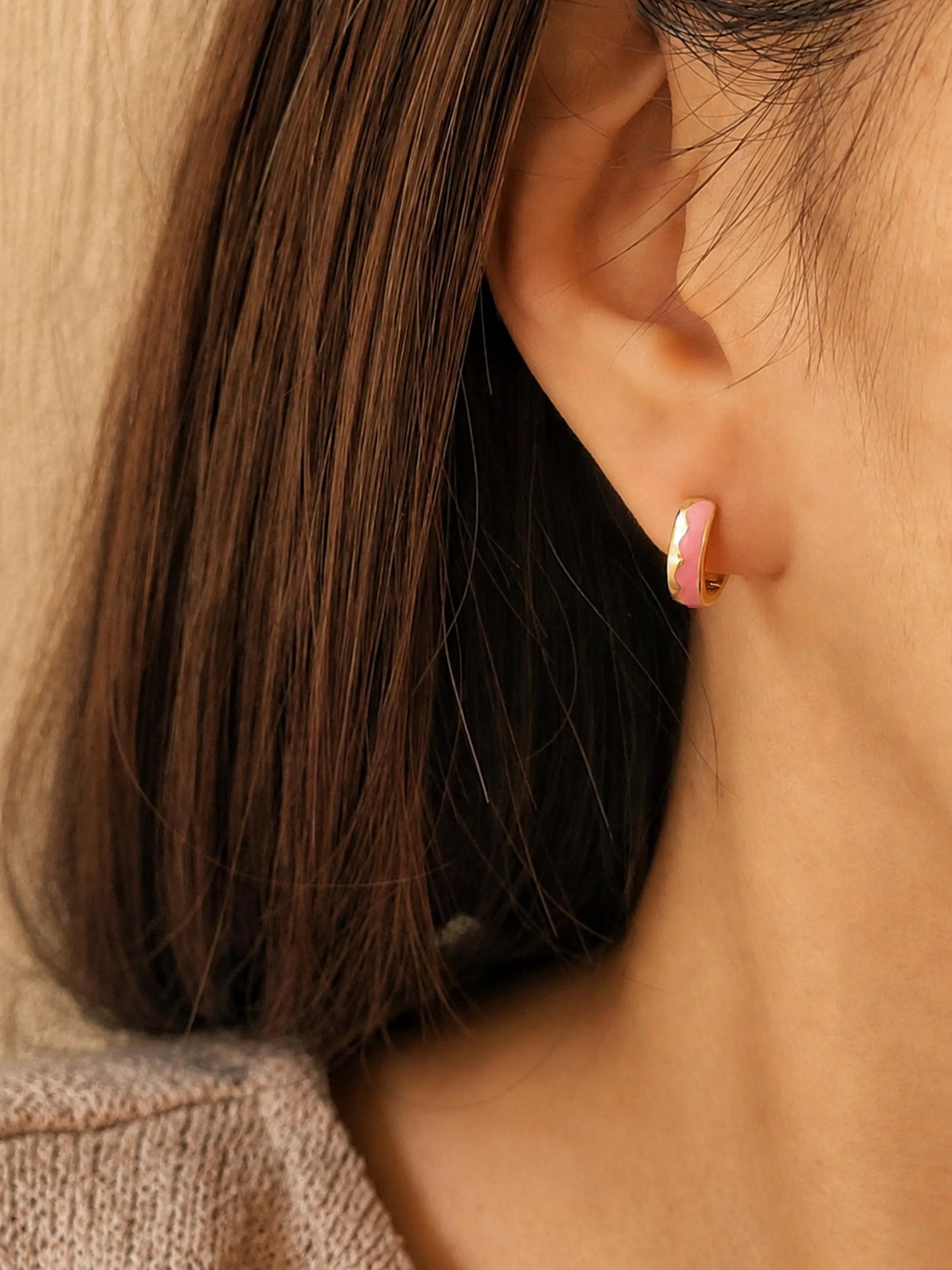 Close up of a woman wearing a pink enamel huggie earrings in gold vermeil featuring glossy wavy pattern. Dainty and minimalist jewellery for everyday wear.
