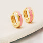 A pair of gold plated huggie hoops with a pink wavy enamel pattern, showcasing a stylish and modern design.