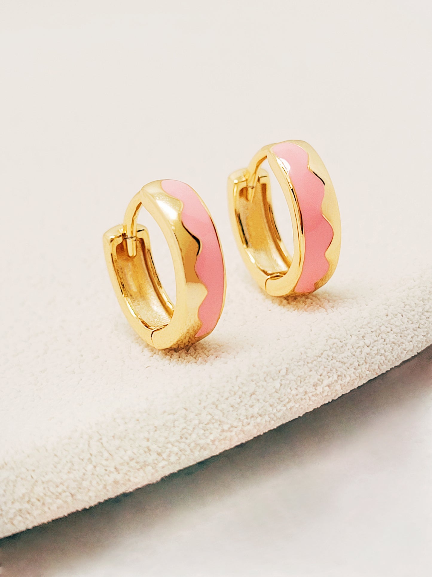 A pair of gold plated huggie hoops with a pink wavy enamel pattern, showcasing a stylish and modern design.