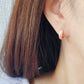 Close-up of a woman’s ear wearing pink and gold enamel huggie earrings, showcasing their smooth finish and playful wavy design.