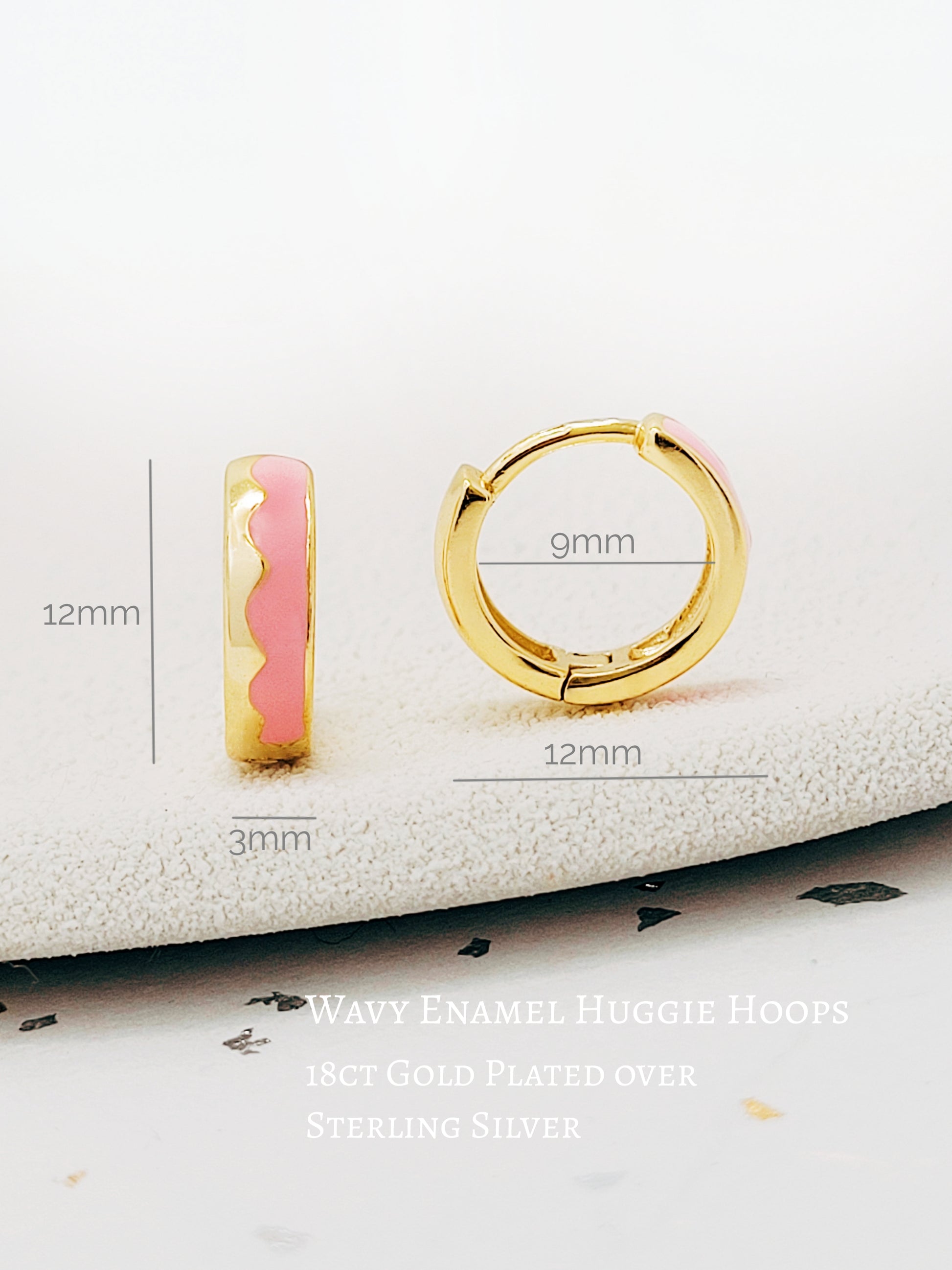 Details of a pair of chic pink enamel huggie hoops with a unique wavy pattern in 18K gold plating, perfect for adding a pop of color.