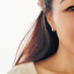 Close-up of a woman’s ear wearing pink and gold enamel huggie earrings, showcasing their smooth finish and playful wavy design.