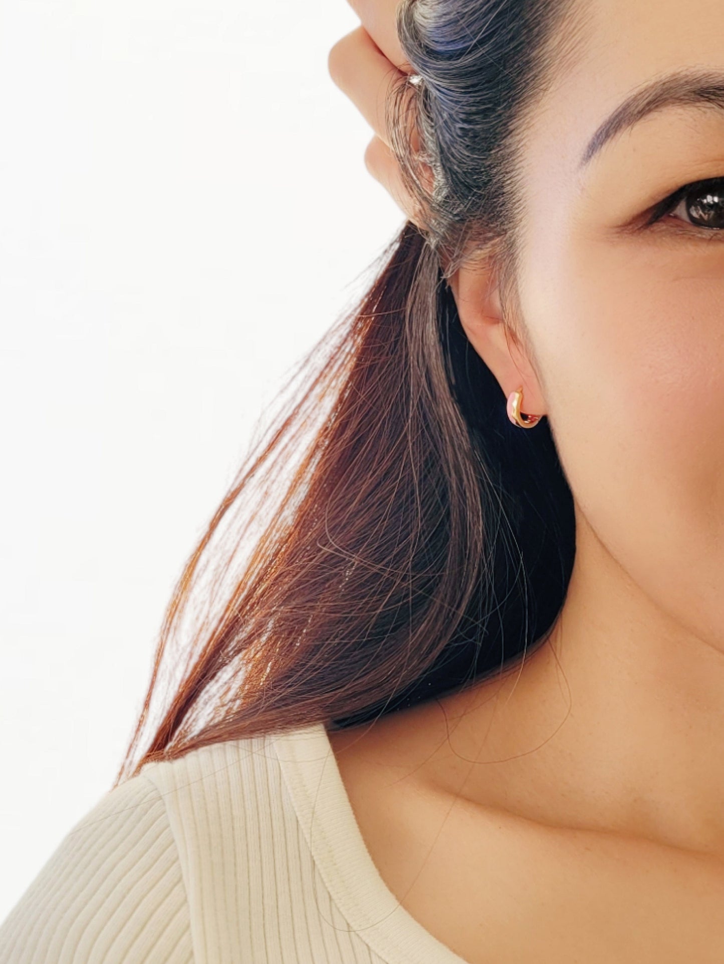 Close-up of a woman’s ear wearing pink and gold enamel huggie earrings, showcasing their smooth finish and playful wavy design.