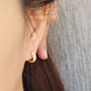 Close-up of a woman’s ear wearing pink and gold enamel huggie earrings, showcasing their smooth finish and playful wavy design.