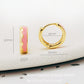 Details of a pair of chic pink enamel huggie hoops with a unique wavy pattern in 18K gold plating, perfect for adding a pop of color.