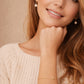 A woman in a cozy white sweater, showcasing a lovely gold pretzel bracelet on her wrist.