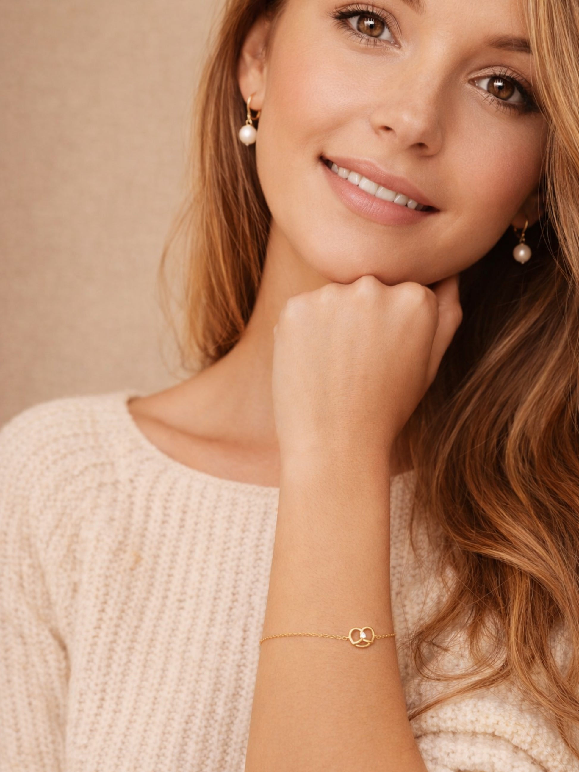 A woman in a cozy white sweater, showcasing a lovely gold pretzel bracelet on her wrist.