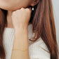 A woman in a cozy white sweater, showcasing a lovely gold pretzel bracelet on her wrist.