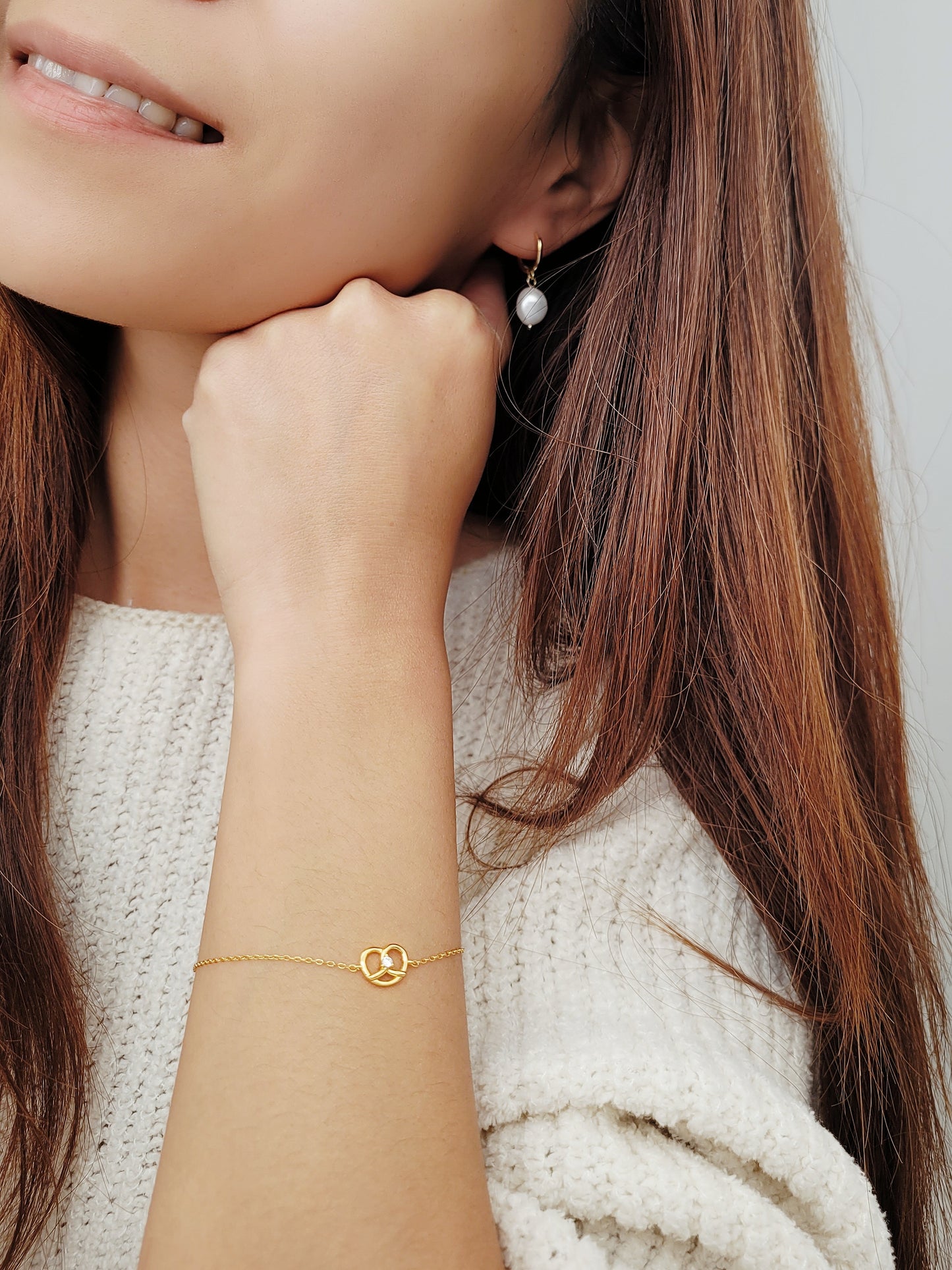 A woman in a cozy white sweater, showcasing a lovely gold pretzel bracelet on her wrist.