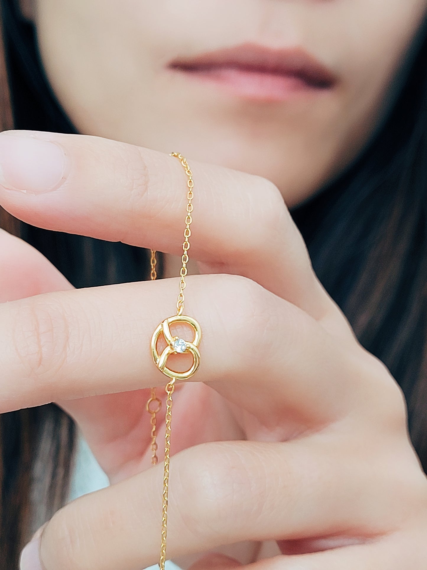 A woman's hand displays a stunning gold pretzel bracelet, emphasizing its lovely craftsmanship and stylish appeal.