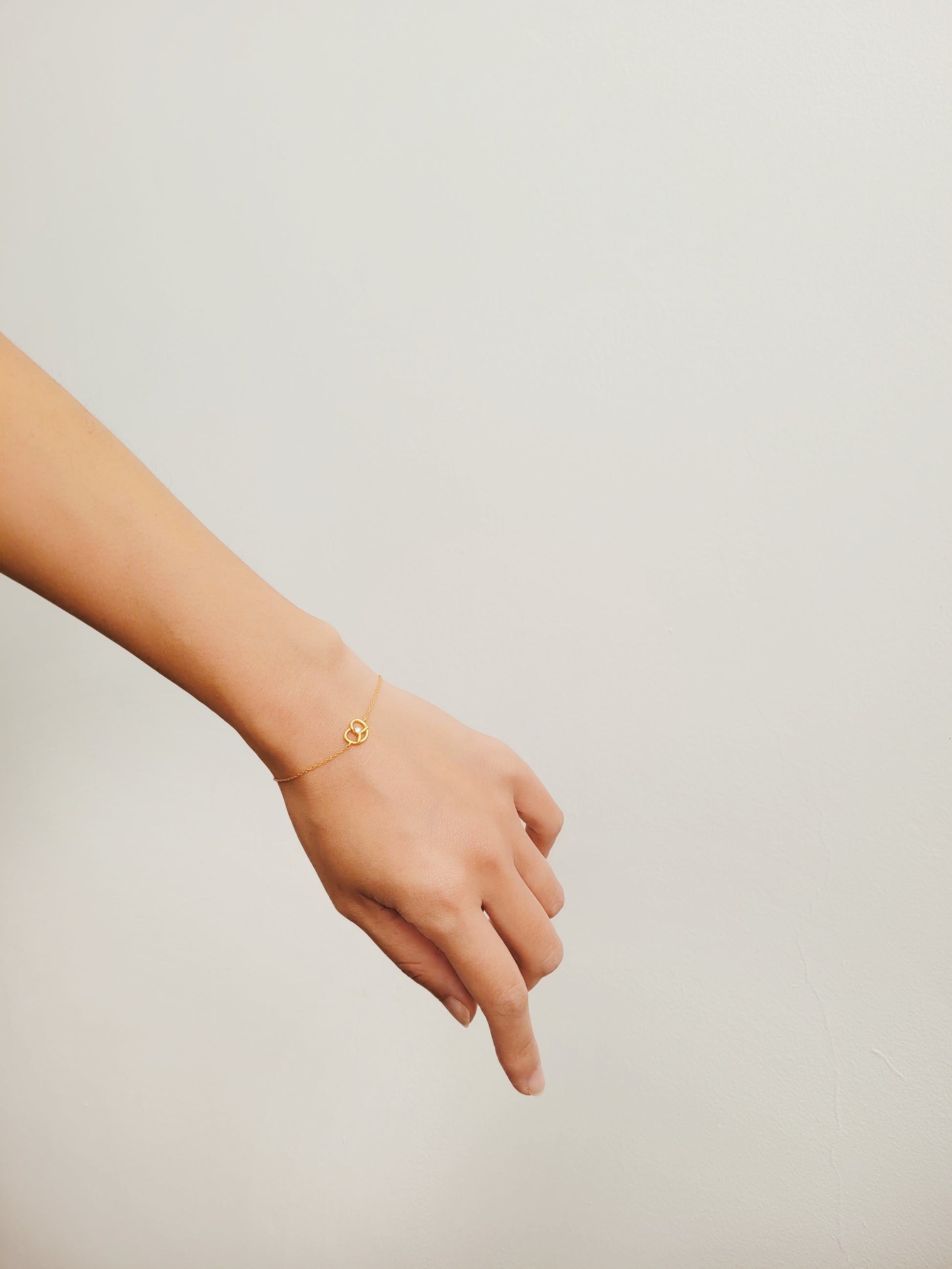 A woman's hand elegantly wears a lovely gold pretzel bracelet, showcasing its unique design and shine.