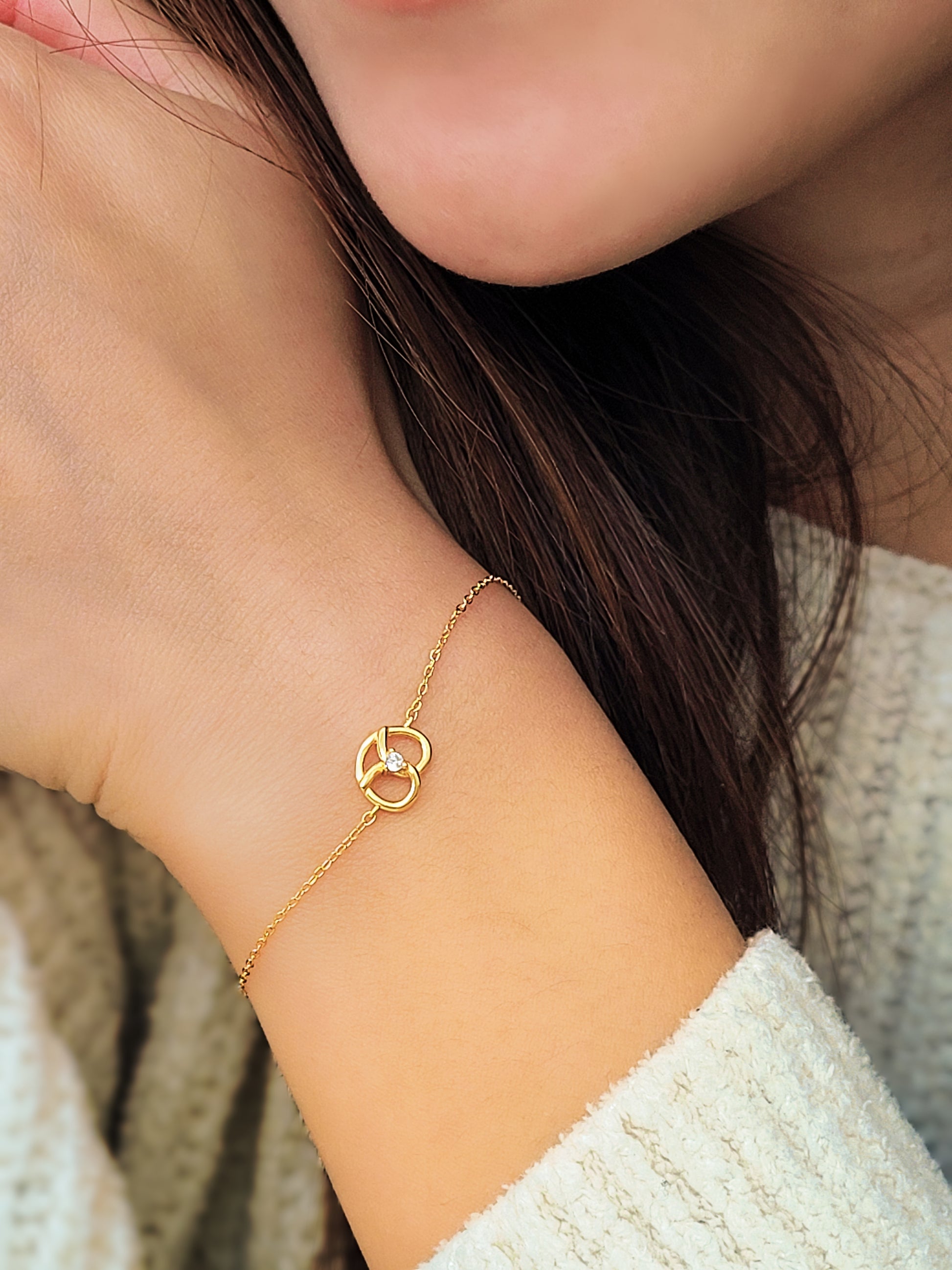 Close-up of a woman's hand gripping a beautiful gold pretzel bracelet, highlighting its intricate details and charm.