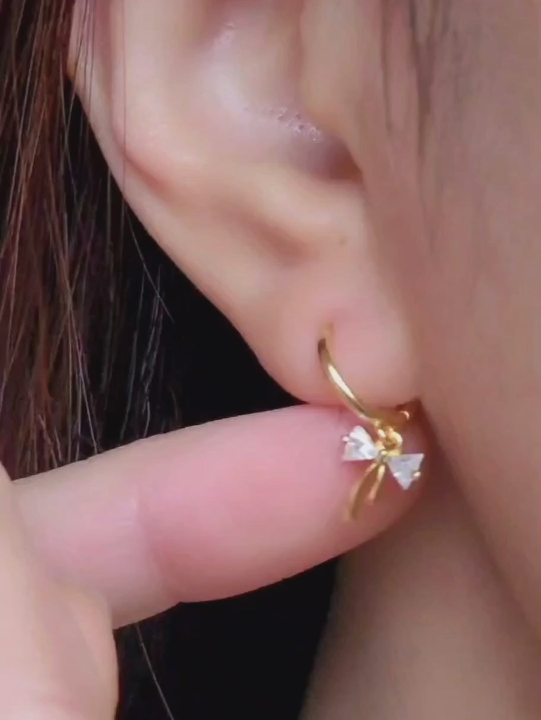 Close-up view of a woman&#39;s ear wearing gold ribbon bow earring with a dangling design, perfect for gifting to girlfriends, daughters, or loved ones.