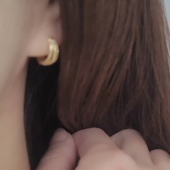 Close up of a woman wearing a minimalist triple hoop twisted huggie earrings crafted in 18k gold plated sterling silver.