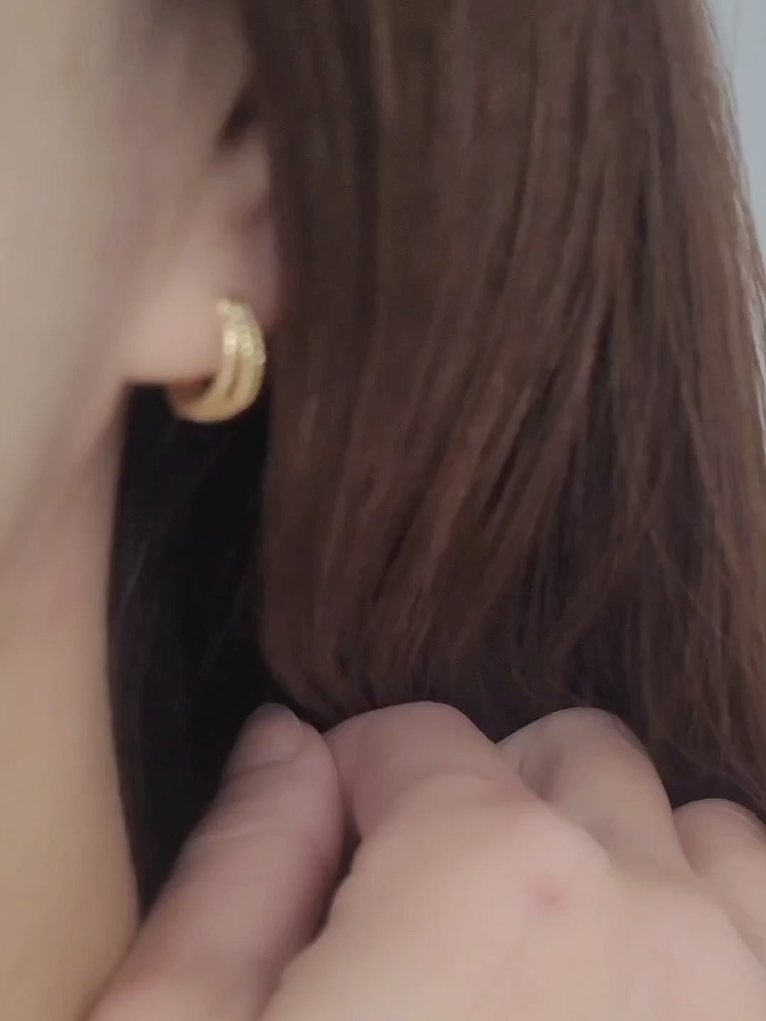 Close up of a woman wearing a minimalist triple hoop twisted huggie earrings crafted in 18k gold plated sterling silver.