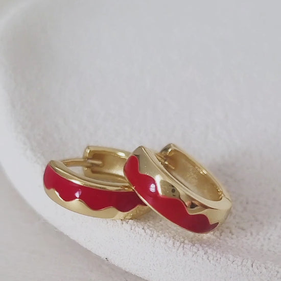 A woman showcasing her trendy red enamel hoop earrings. 