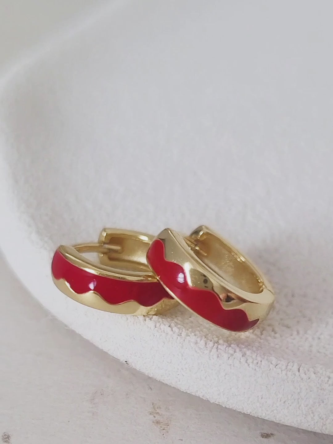 A woman showcasing her trendy red enamel hoop earrings. 