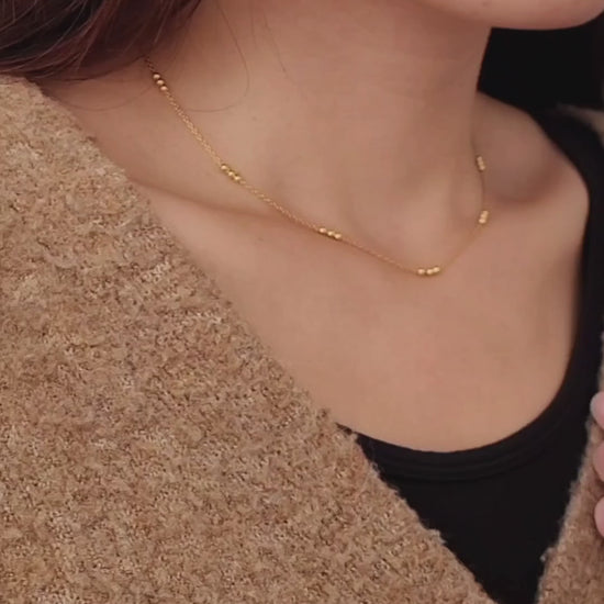 Close-up of a woman wearing a delicate 18ct gold vermeil triple ball necklace, showcasing its minimalist design with small gold beads spaced along a fine chain.