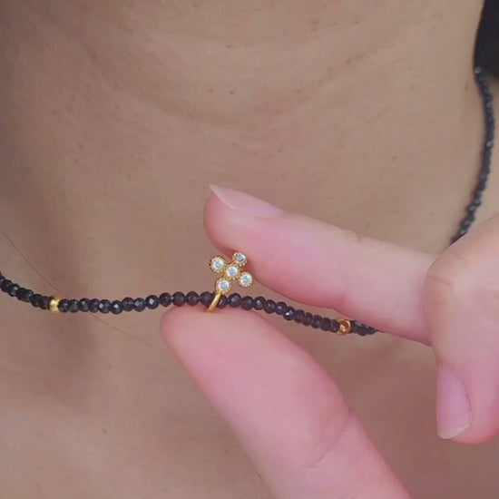 Close-up of a woman wearing an edgy black spinel beaded necklace with a mini clover pendant in gold.