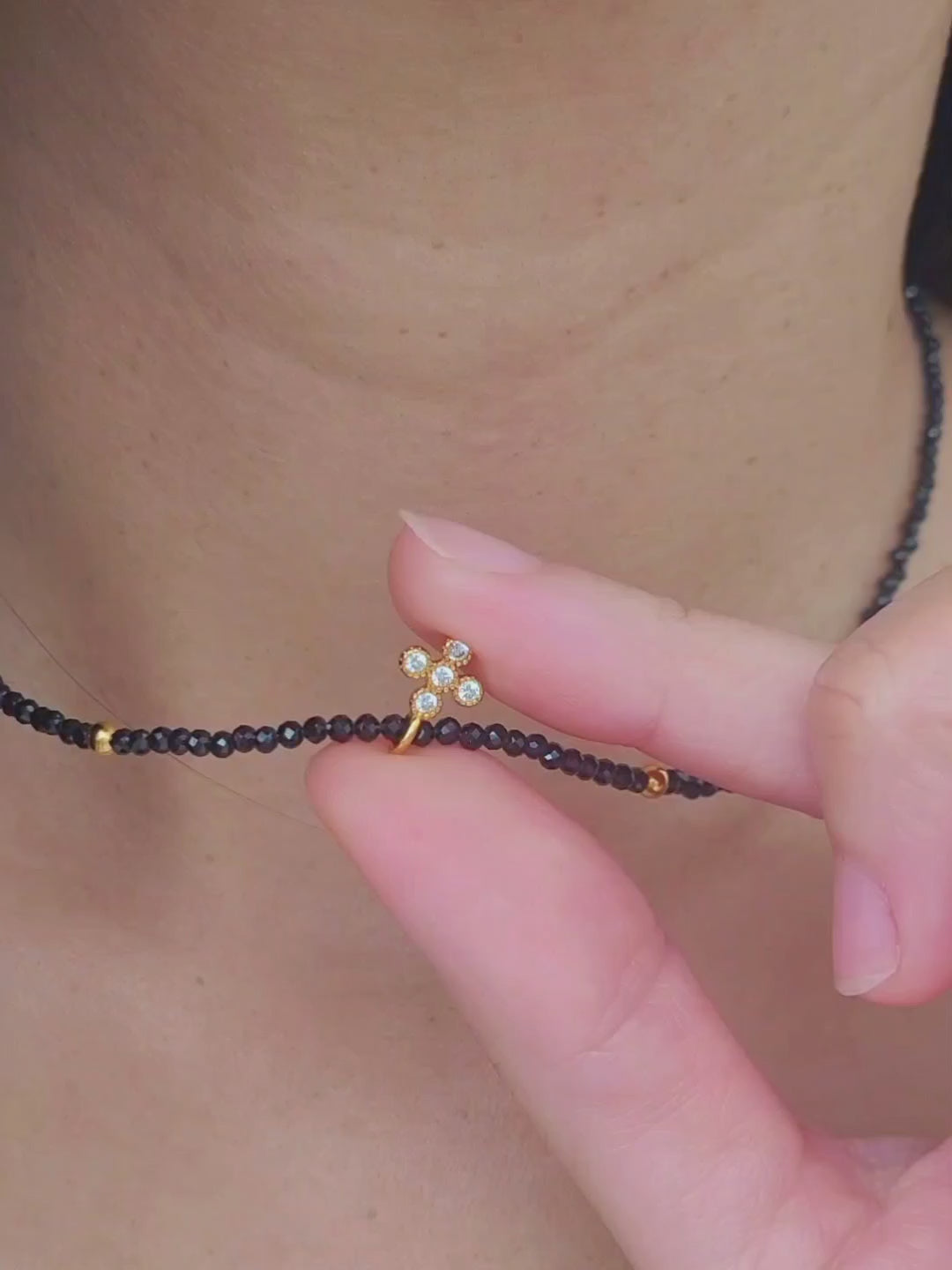 Close-up of a woman wearing an edgy black spinel beaded necklace with a mini clover pendant in gold.