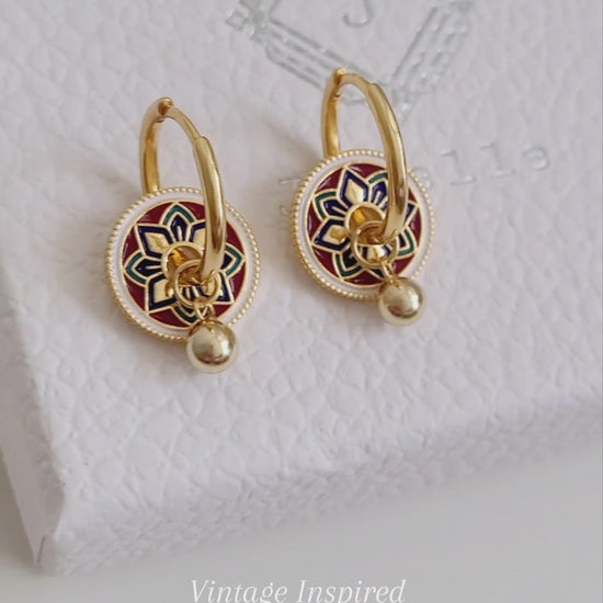 Gold hoop earrings featuring a tile pattern disc and a gold ball dangle, displayed on a white surface showcasing their elegant and unique artisan design.